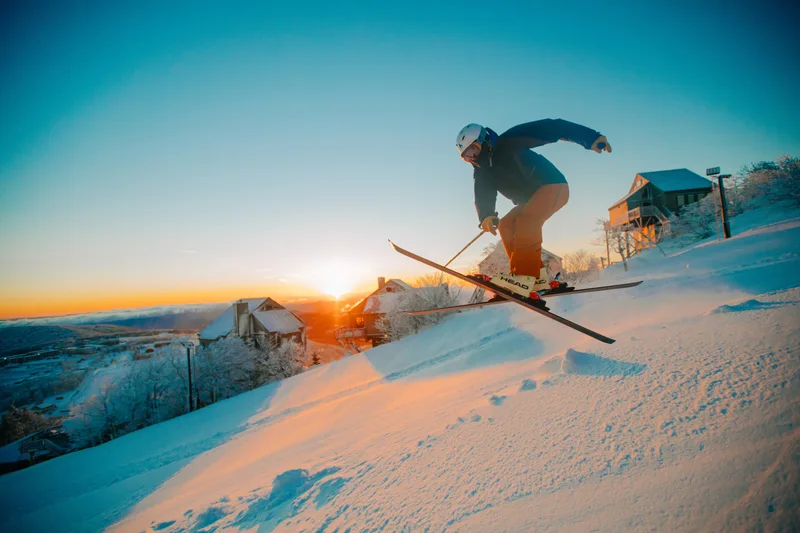 A skier at Beech Mountain with sunlit snow and mountain views at sunset